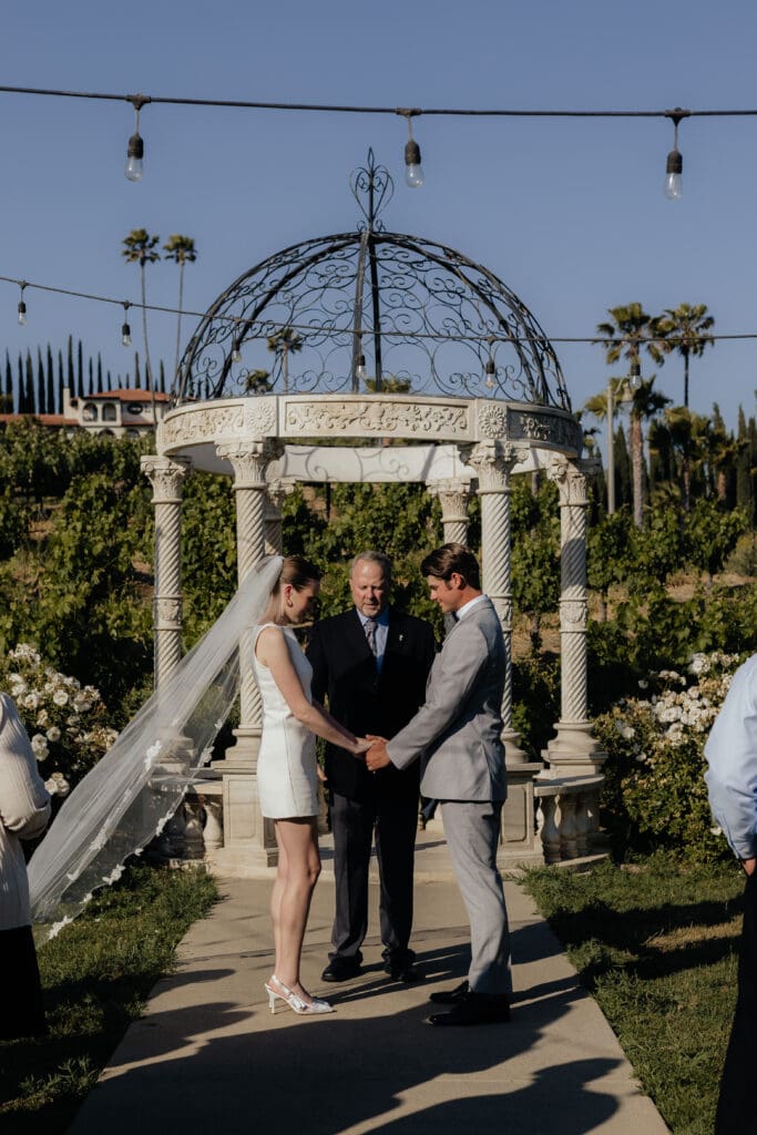 Evan & Payton standing with their officiant praying together during their cereomy.