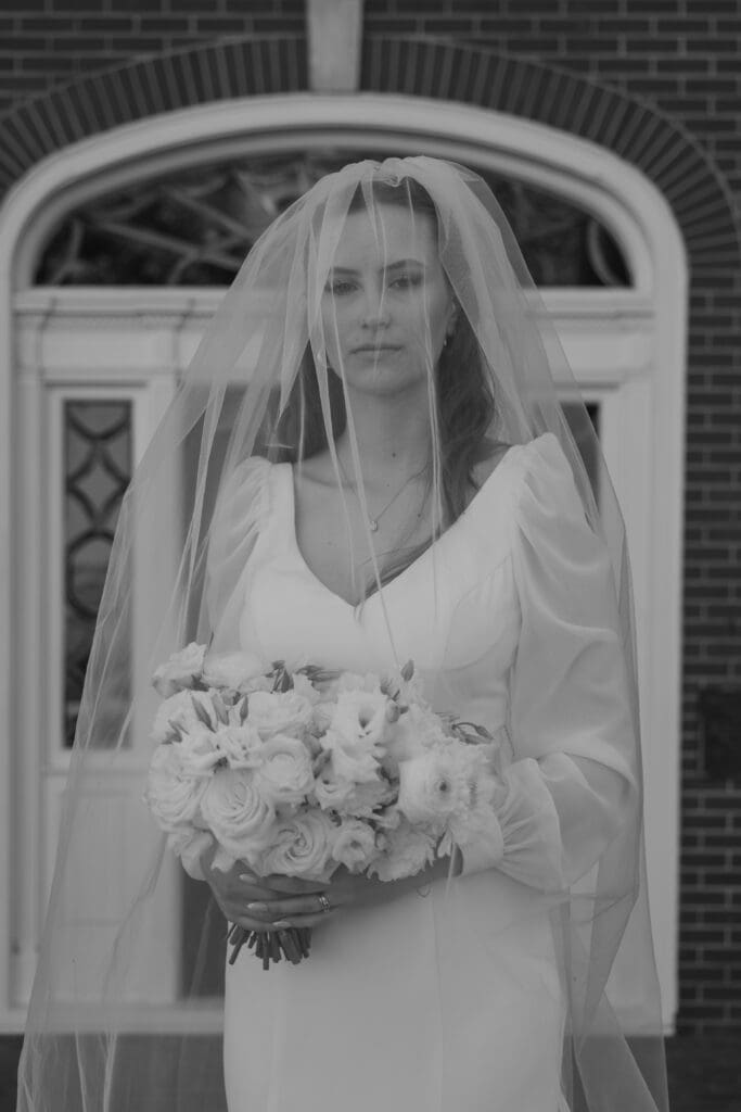 Bride with veil over her face holding her bouquet, in black and white.